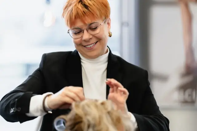 Lächelnde Stylistin arbeitet mit Wicklern im Haar einer Kundin bei Kaiserreich Hairstyle in Nürnberg