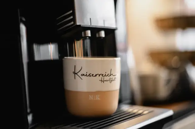 Kaiserreich-Kaffeebecher neben einer Kaffeemaschine bei Kaiserreich Hairstyle in Nürnberg