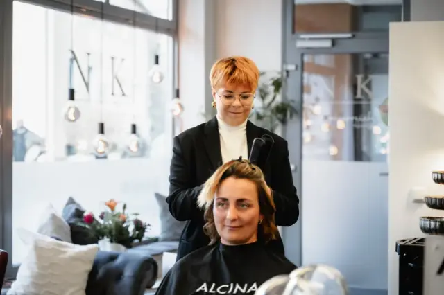 Stylistin arbeitet hinter einer brünetten Kundin am Spiegel bei Kaiserreich Hairstyle in Nürnberg
